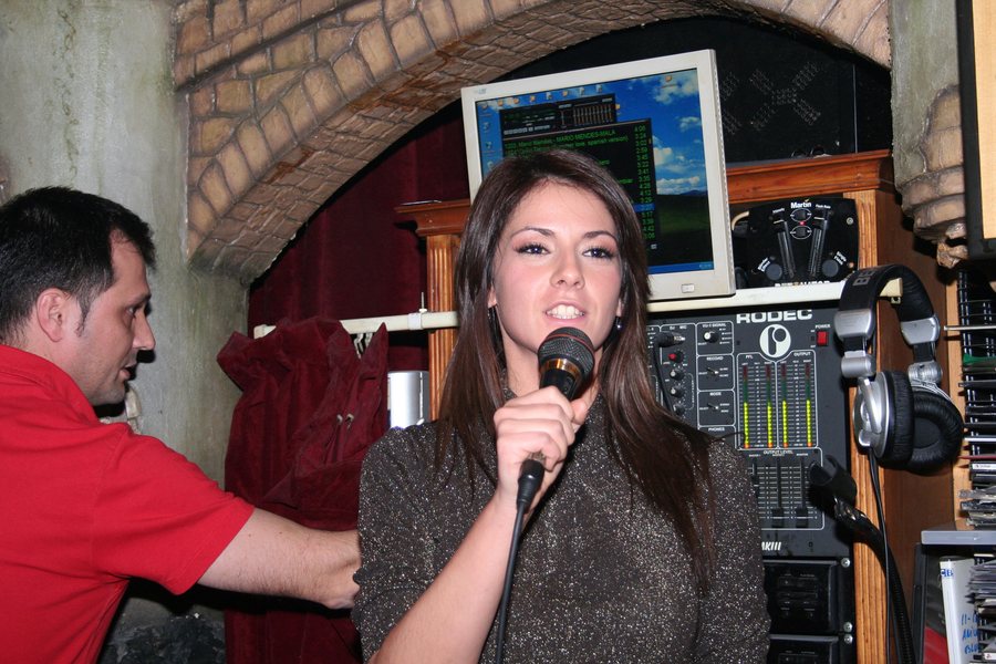 Jael Geijo presentando el evento con un micrófono, junto a la cabina del disc-jockey.